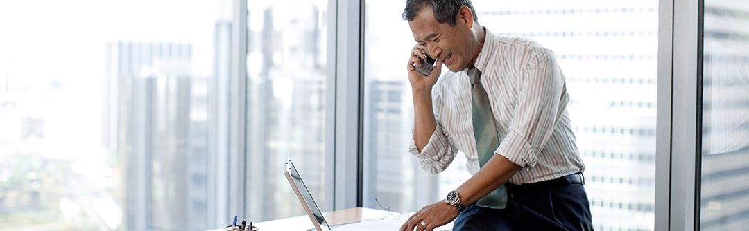 Man sitting on desk in a high-rise office building talking on a cell phone